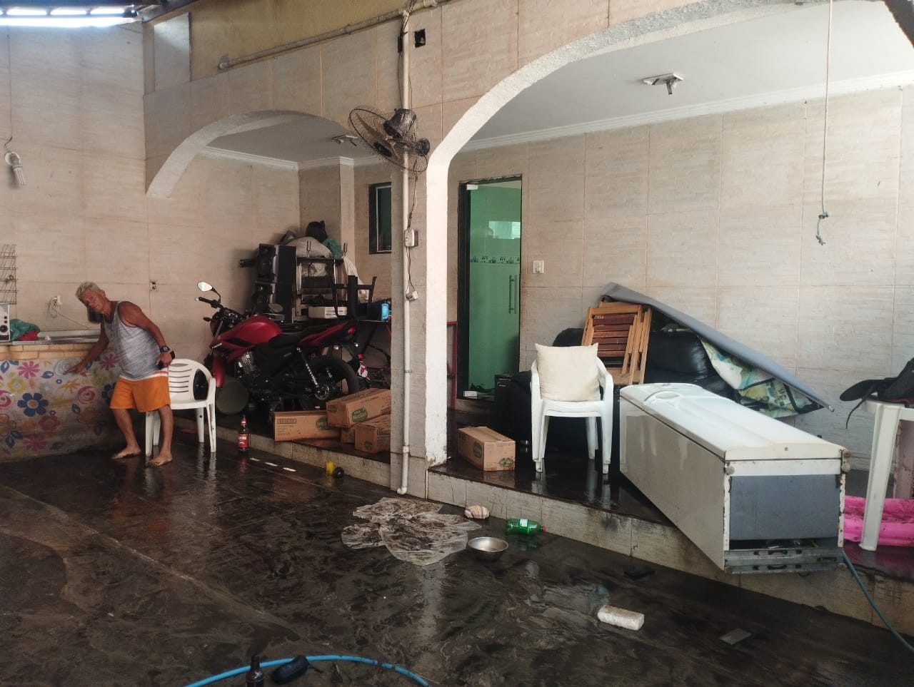 O comerciante Robson Machado mostra até que ponto a água chegou na garagem da casa da sua mãe em Santíssimo, na Zona Oeste do Rio 