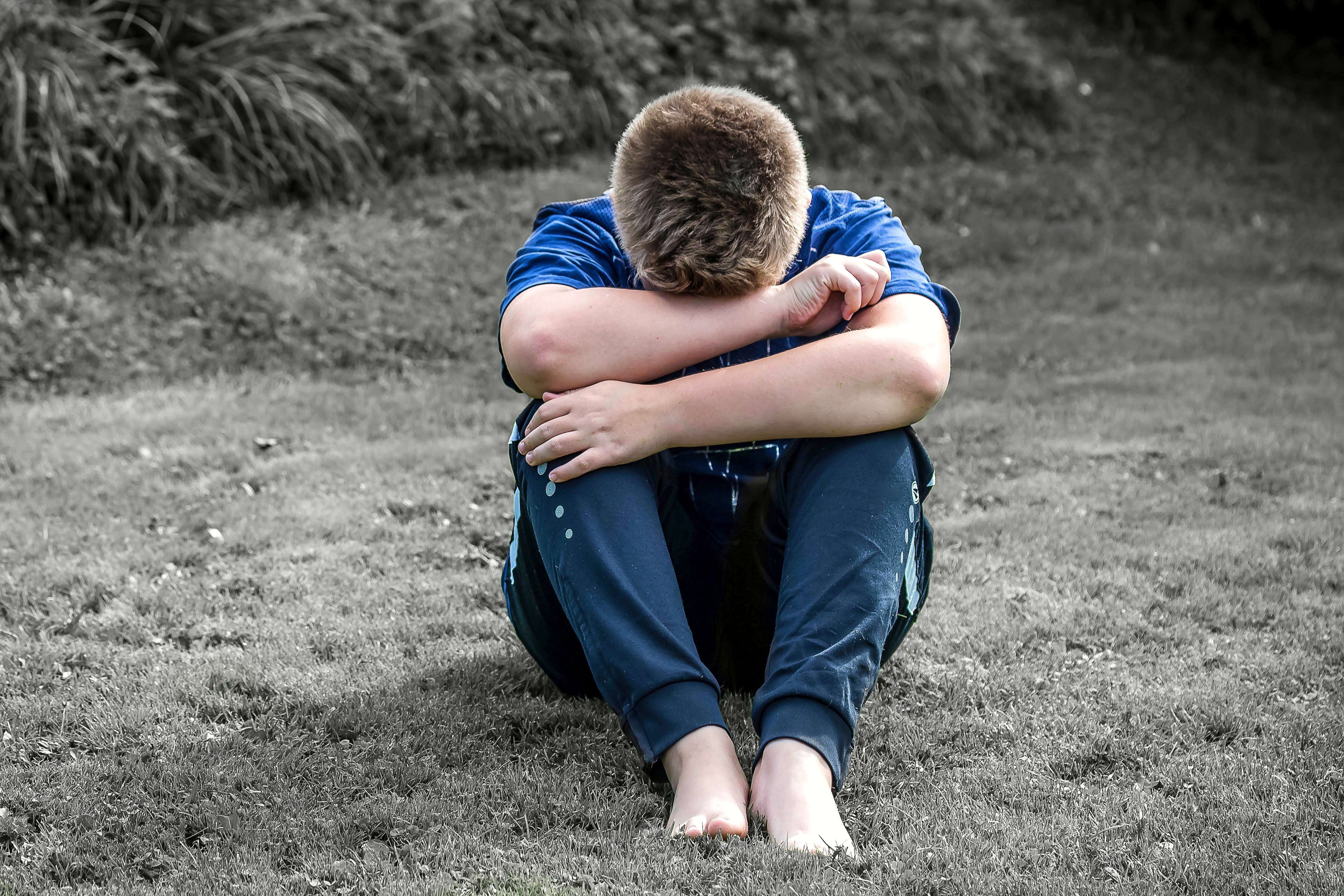 Menino sentado na grama e encolhido (Foto: Pixabay/Pexels)