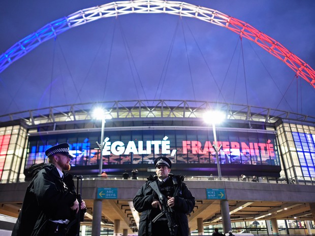 Policiais armados são vistos em frente ao estádio Wembley, em Londres, antes do amistoso entre Inglaterra e França; Ao fundo é possível ver o estádio iluminado com as cores da bandeira francesa e o lema 'Liberdade, Igualdade, Fraternidade'  (Foto: Dylan Martinez/Livepic/Reuters)
