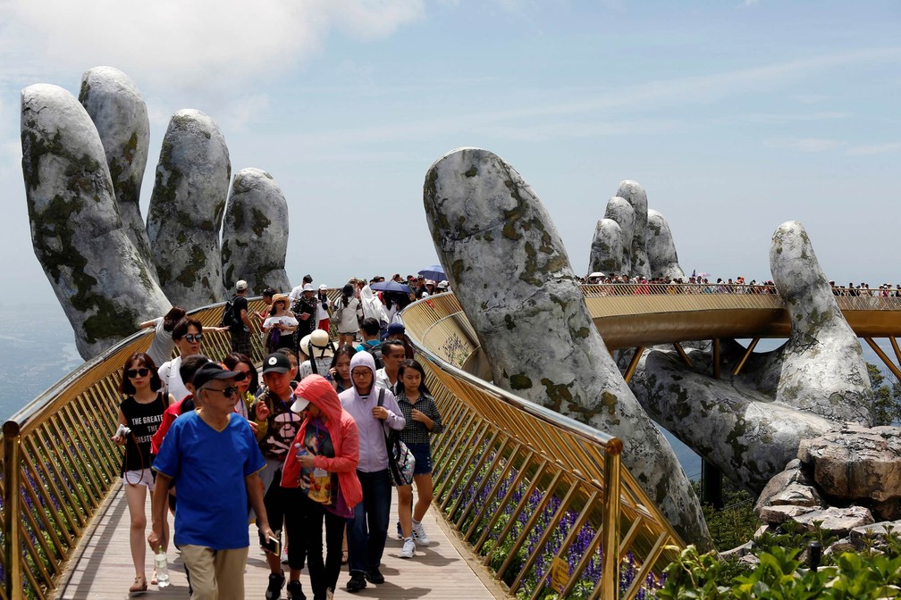 Turistas passeiam pela Ponte Dourada, ponto turístico no monte Ba Na perto da cidade de Danang, no Vietnã. A ponte tem duas enormes esculturas em forma de mão como parte da sustentação de sua estrutura — Foto: Kham/Reuters