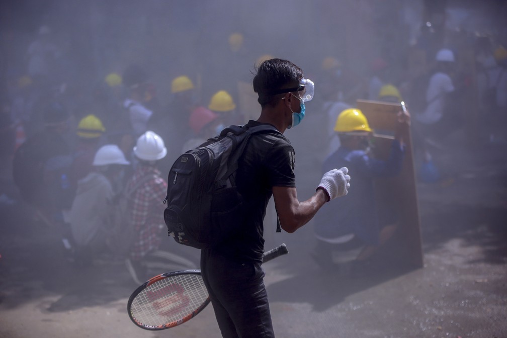 Manifestante contra o golpe militar em Mianmar segura uma raquete de tênis em meio a fumaça de bombas de gás jogadas pela polícia durante protesto em Yangon em 4 de março de 2021 — Foto: AP