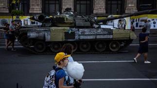 Menino come algodão doce ao lado de tanque de guerra russo destruído que foi transformado em museu, na rua Khreshchatyk, em Kiev  — Foto: DIMITAR DILKOFF / AFP