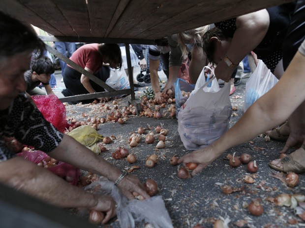 Gregos recolhem cebolas caídas no chão durante a distribuição de comida (Foto: Reuters/John Kolesidis)