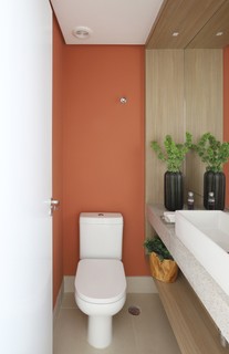 No lavabo, a parede colorida em um tom alaranjado traz unidade aos tons neutros do piso, metais e bancada. Projeto do escritório Studio Vista Arquitetura