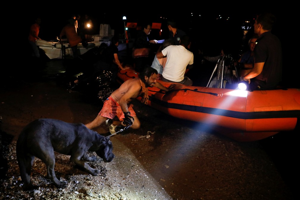 Homem puxa um cão para um bote durante evacuação de área atingida por incêndio na Grécia (Foto: Alkis Konstantinidis / Reuters)