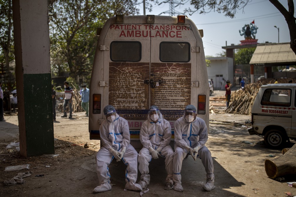 Trabalhadores de saúde exaustos sentam-se no degrau traseiro de uma ambulância após carregar mortos para cremação em Nova Délhi, na Índia, em 24 de abril de 2021 — Foto: Altaf Qadri/AP