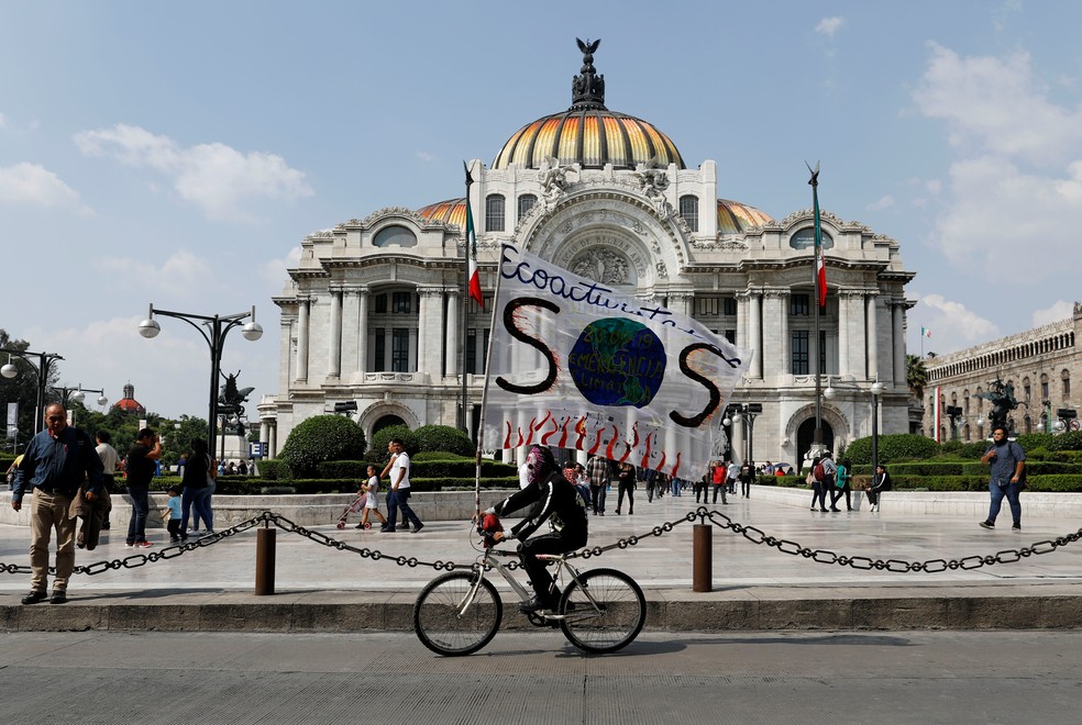 Ciclista leva cartaz contra mudanças climáticas na Cidade do México, em frente ao Palácio de Belas Artes. — Foto: REUTERS/Carlos Jasso