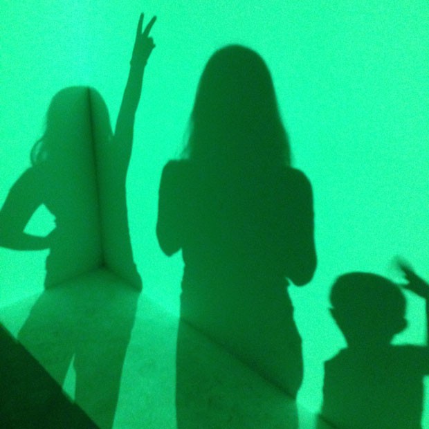 Sombra da Giullia, minha e do Lorenzo (da esq. para a dir.), na obra Raethro Green, do artista de James Turrell. Trata-se de uma projeção de luz verde em um canto da sala (Foto: Arquivo Pessoal/Cristiane Marangon)
