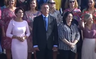A primeira-dama Michelle Bolsonaro, o presidente Jair Bolsonaro e a ministra da Mulher, da Família e dos Direitos Humanos, Damares Alves, acompanham apresentação da banda marcial durante hasteamento da bandeira em Brasília (Foto: Reprodução/TV Brasil)