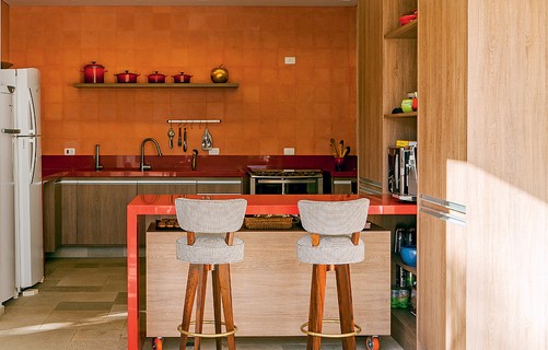 A parede da cozinha tem ladrilho hidráulico rosa-claro. Cercado por outros elementos laranjas, ele reflete a cor. Projeto do escritório Arkitito