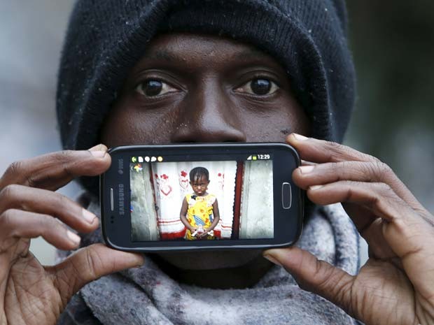 Papi, de Kinshasa, no Congo, mostra foto da filha Gisele ao esperar na froteira da Eslovênia com a Áustria (Foto: REUTERS/Srdjan Zivulovic)