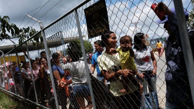 Pessoas formam fila atrás de grade em Paracaraima; recursos para acolhimento de venezuelanos estão garantidos apenas até março deste ano (Foto: Reuters via BBC News Brasil)