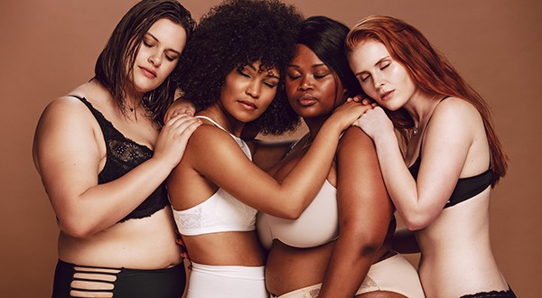Different size females in lingerie hugging each other with their eyes closed. Multi-ethnic women of different weight in underwear together on brown background. (Foto: Getty Images/iStockphoto)