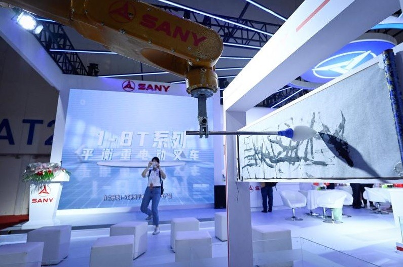 Uma mulher usa seu celular para tirar uma foto de um braço robótico pintando uma tela — Foto: Wang Zhao / AFP