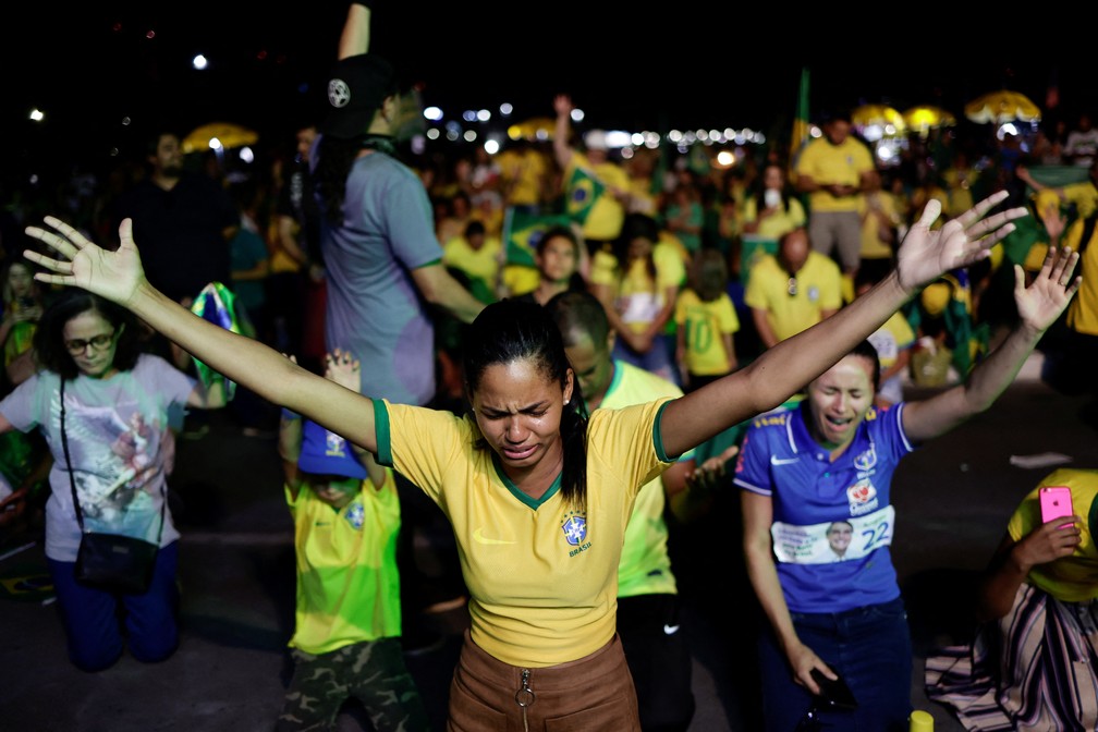 Vestido com camisas da seleção brasileira, apoiadores rezam durante apuração em Brasília.  — Foto: REUTERS/Ueslei Marcelino