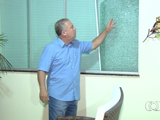 Prefeito de Senador Canedo, Misael Oliveira mostra janela danificada por tiro, em Goiás (Foto: Reprodução/TV Anhanguera)