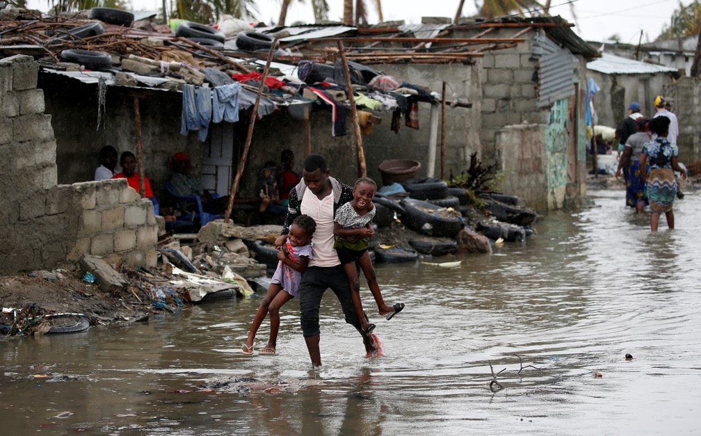 Homem carrega crianças em área inundada na cidade de Beira, Moçambique, neste domingo (24). — Foto: Reuters/Siphiwe Sibeko
