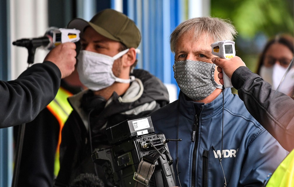 Segurança controla temperatura de jornalistas na entrada da fábrica da Ford em Colônia, na Alemanha. Montadora norte-americana reinicia a produção nesta segunda-feira (4)  — Foto: Martin Meissner/AP 