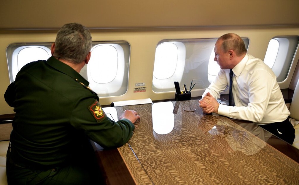 Putin senta-se a frente do ministro da Defesa dentro do avião presidencial em foto de arquivo — Foto: Kremlin via AP