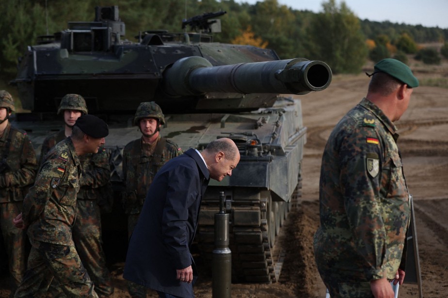 O chanceler alemão Olaf Scholz  abaixando a cabeça enquanto passa por um tanque de batalha  Leopard 2 das Forças Armadas alemãs durante um exercício de treinamento no campo militar em Ostenholz, Norte da Alemanha.