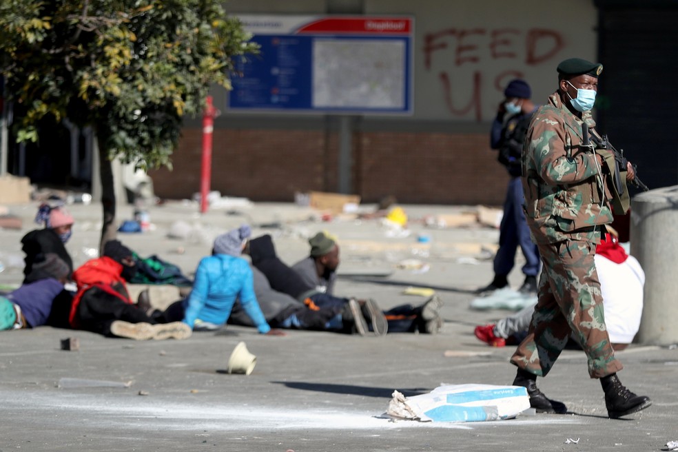 Militar mant&eacute;m guarda pr&oacute;ximo a suspeitos de saque do lado de fora do shopping Diepkloof, em Soweto, nesta ter&ccedil;a (13), ap&oacute;s &agrave; pris&atilde;o do ex-presidente sul-africano Jacob Zuma &mdash; Foto: Siphiwe Sibeko/Reuters