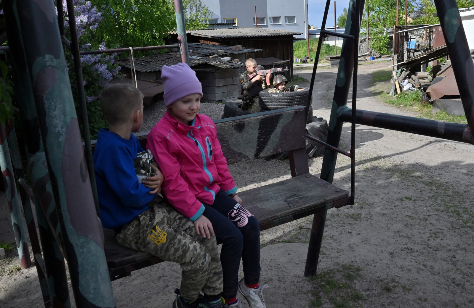 Crianças conversam em parque enquanto outra 'brinca' de guerra, nos arredores de Kiev — Foto: Sergei Supinsky/AFP