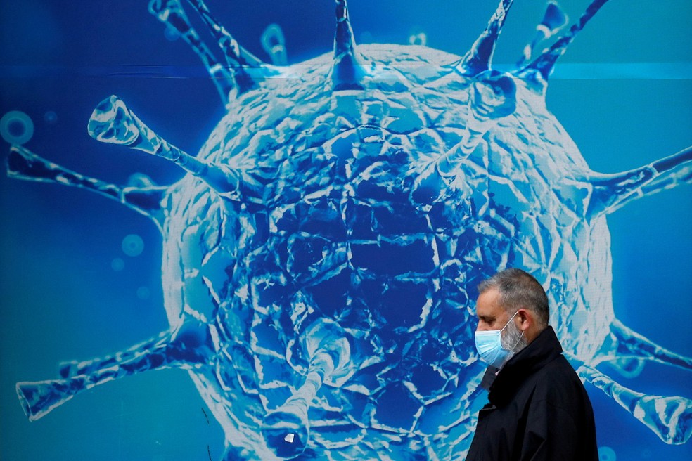 Homem usando máscara passa em frente a ilustração do coronavírus em Oldham, no Reino Unido — Foto: Phil Noble/Reuters
