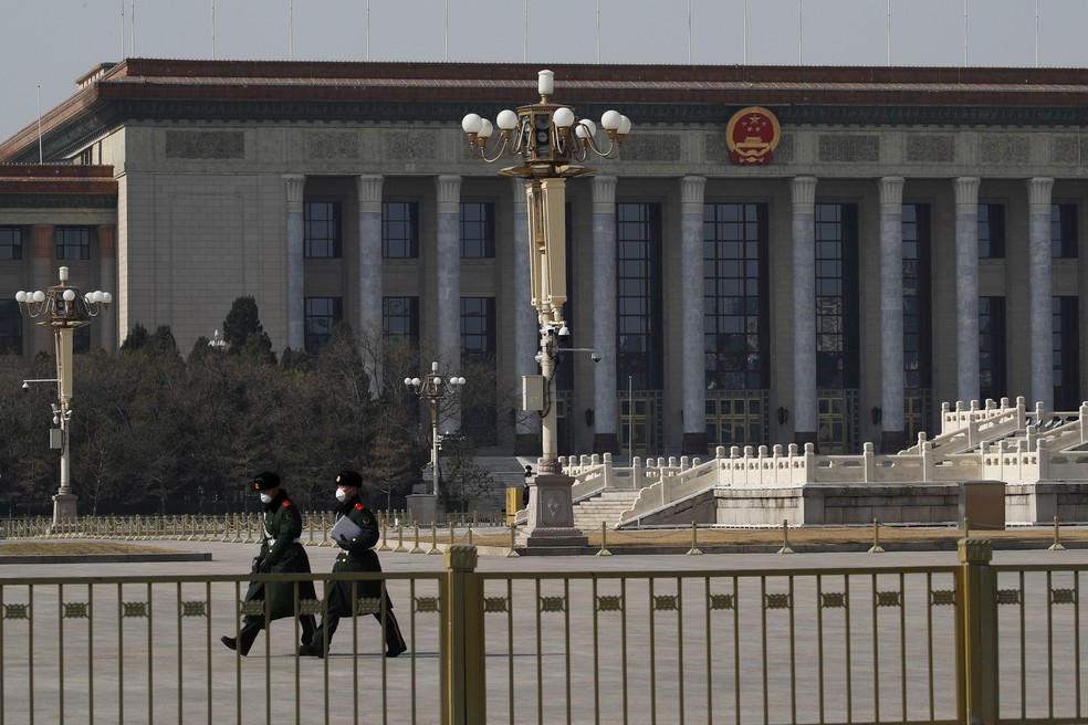 Policiais com máscaras caminham pela Praça Tiananmen, em frente ao edifício parlamentar de Pequim. China anunciou nesta segunda-feira(24) que adiou sua reunião política mais importante do ano. — Foto: Andy Wong/AP
