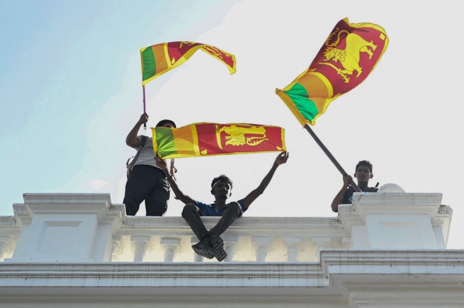 Manifestantes agitam bandeiras do Sri Lanka de uma varanda dentro do prédio de escritórios do primeiro-ministro durante um protesto contra o governo em Colombo