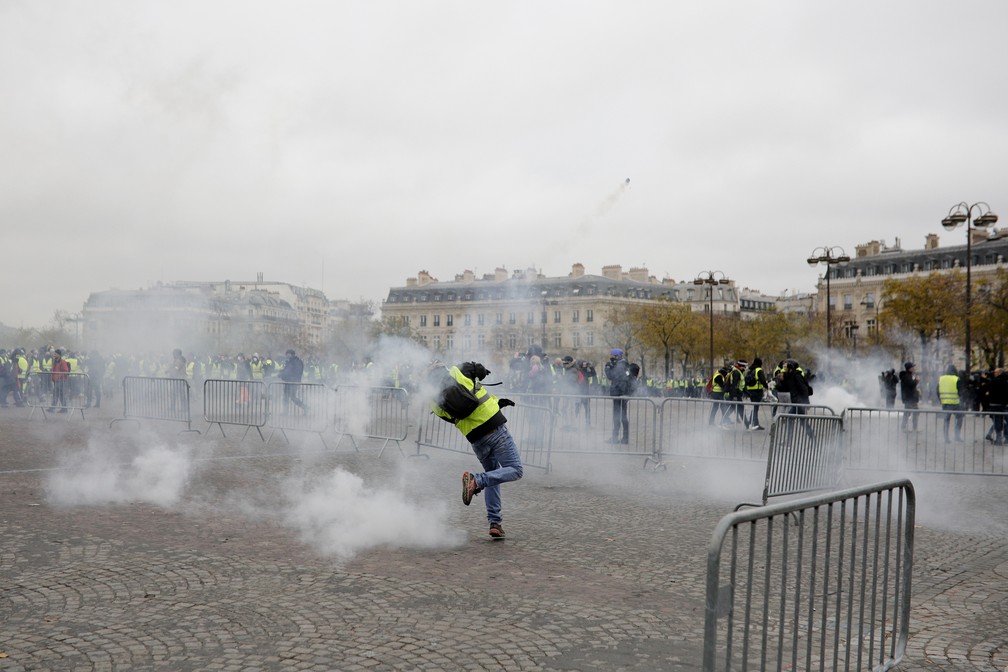 Manifestante de colete amarelo lança gás contra a polícia neste sábado (1) na avenida Champs-Elysées, em Paris. O protesto é contra o aumento de impostos do governo Macron. — Foto:  Kamil Zihnioglu/AP