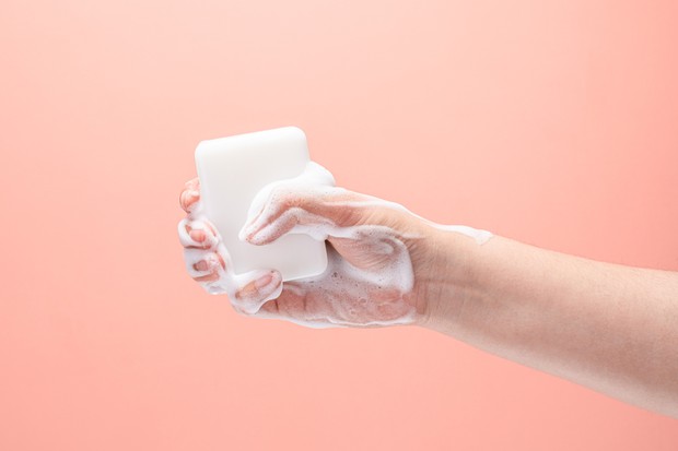 Hand Gripping a White Soap with White Colored Soap Sud on Pink Colored Background. (Foto: Getty Images)