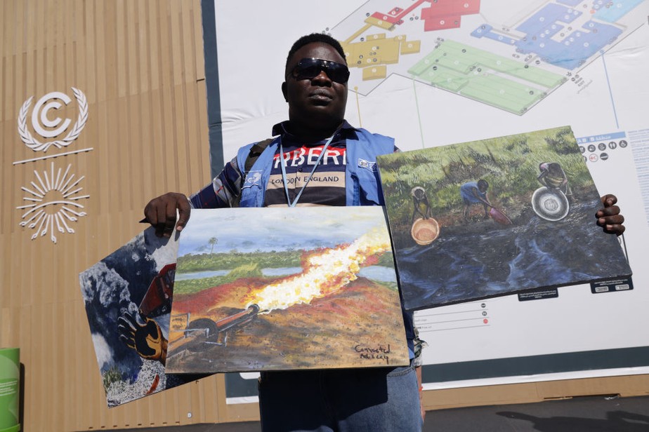 Homem protesta contra a exploração de combustíveis fósseis e segura pinturas de derramamentos de óleo e incêndios em sua região natal, no Delta do Níger, durante COP27