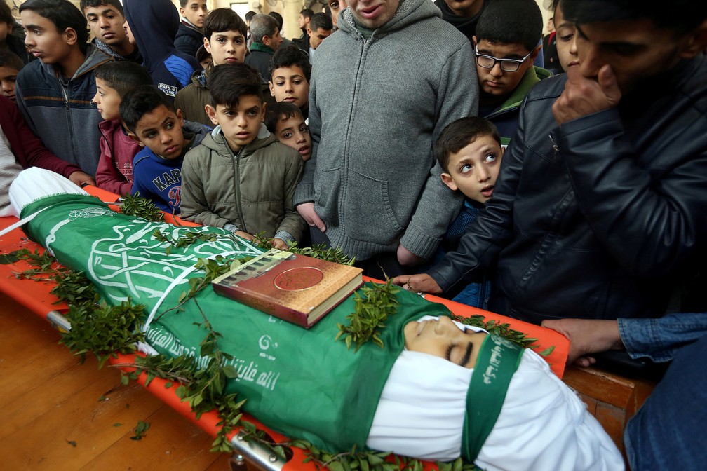 14 de janeiro - Meninos palestinos se aglomeram ao redor do corpo do jovem Abdul Rauf Salha durante seu funeral no norte da Faixa de Gaza. Segundo a mídia local, o adolescente não resistiu aos ferimentos e morreu três dias depois de ser alvejado por soldados israelenses durante confronto na divisa entre Gaza e Israel — Foto: Ibraheem Abu Mustafa/Reuters