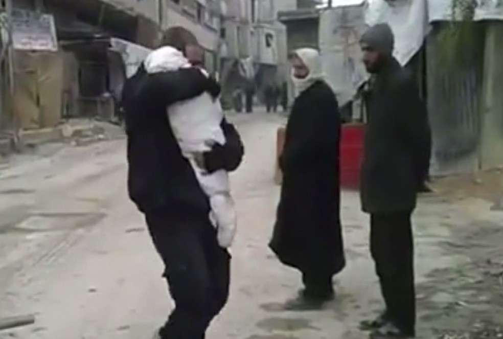 Imagem tirada de vídeo divulgado no dia 21 de fevereiro de 2018 pelo grupo sírio opositor Ghouta Media Center e autenticado pela Associated Press mostra homem abraçado ao corpo de seu filho morto durante bombardeios em Guta Oriental, perto de Damasco  (Foto: Ghouta Media Center via AP)