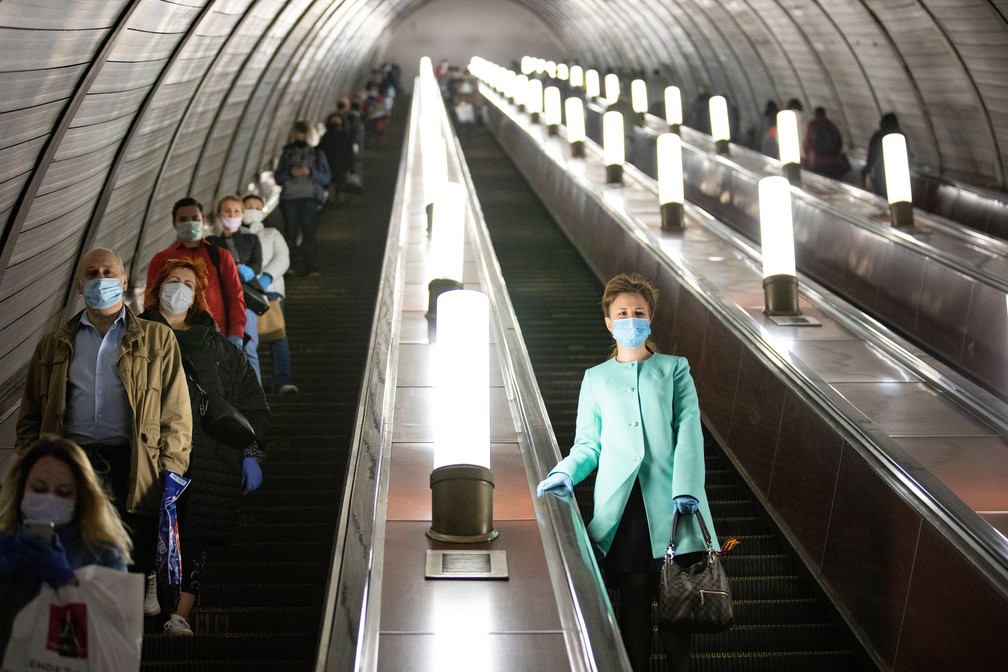 Russos usam luvas e máscaras enquanto andam de escadas rolantes que dão acesso ao metrô de Moscou, na Rússia, na terça-feira (12)  — Foto: Alexander Zemlianichenko/AP 