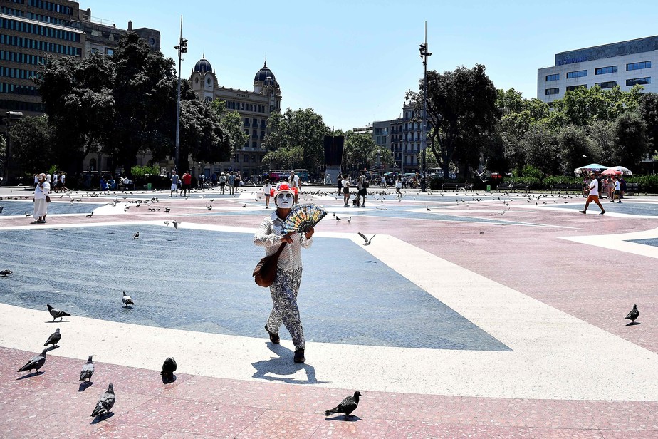 Mulher caminha com leque na mão em Barcelona, a segunda maior cidade da Espanha FOTO: Pau BARRENA / AFP)