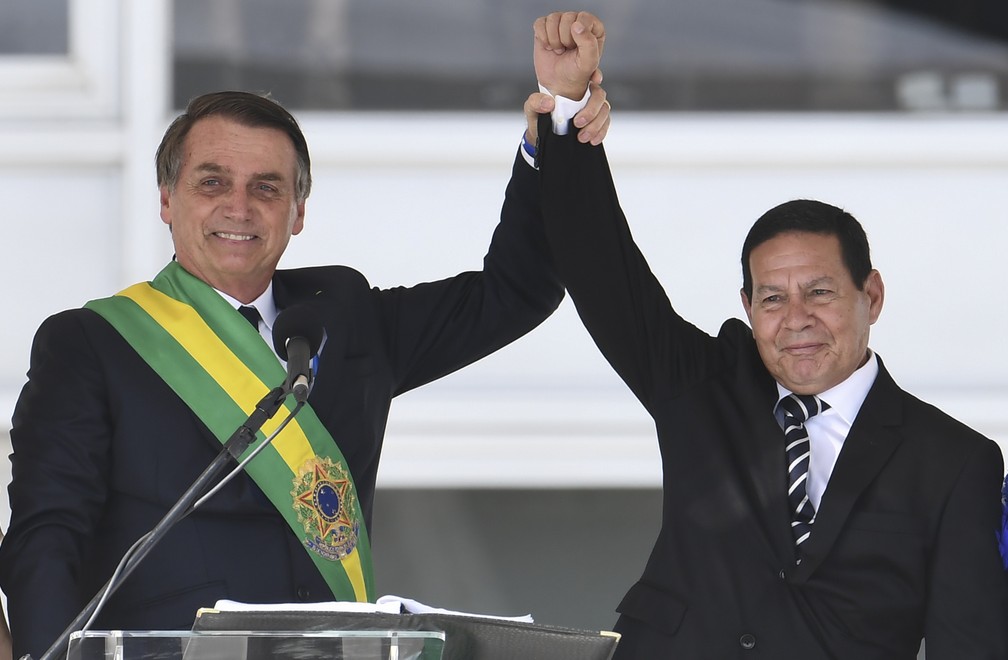 O novo presidente do Brasil, Jair Bolsonaro, e o novo vice-presidente, general Hamilton Mourão, erguem as mãos após discurso no parlatório do Palácio do Planalto — Foto: Evaristo Sá/AFP