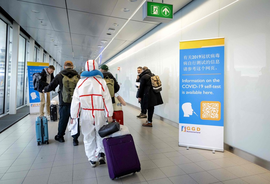 Passageiros vindos da China caminham ao lado de avisos sobre novos controles de entrada em aeroporto na Holanda nesta quarta-feira