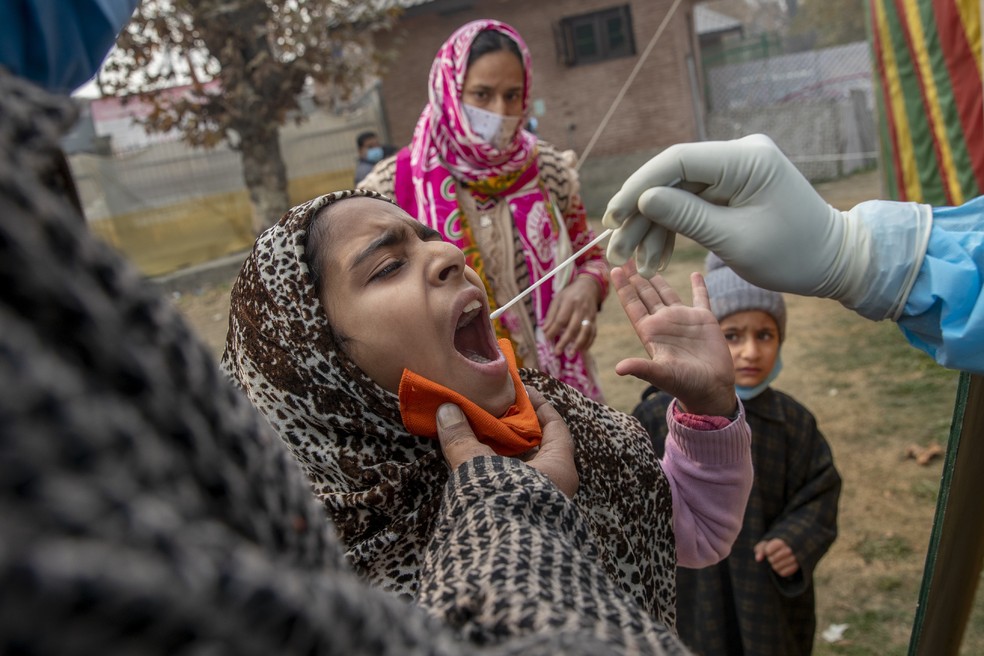 Mulher segura a sua filha enquanto profissional de saúde usa um swab para coletar saliva para um teste de Covid-19 em Srinagar, na Índia — Foto: Dar Yasin/AP