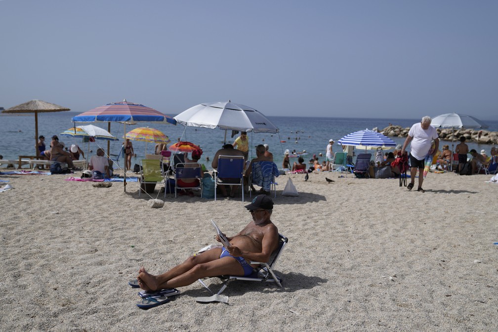 Um homem lê um jornal na praia pública de Alimos, no sul de Atenas, na Grécia (23/06/22). — Foto: AP Photo/Thanassis Stavrakis