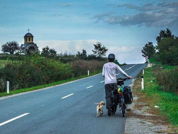 O administrador de redes Thiago Ruiz, de bicicleta e na companhia de um cachorro, na Sérvia (Foto: Diocá/Divulgação)