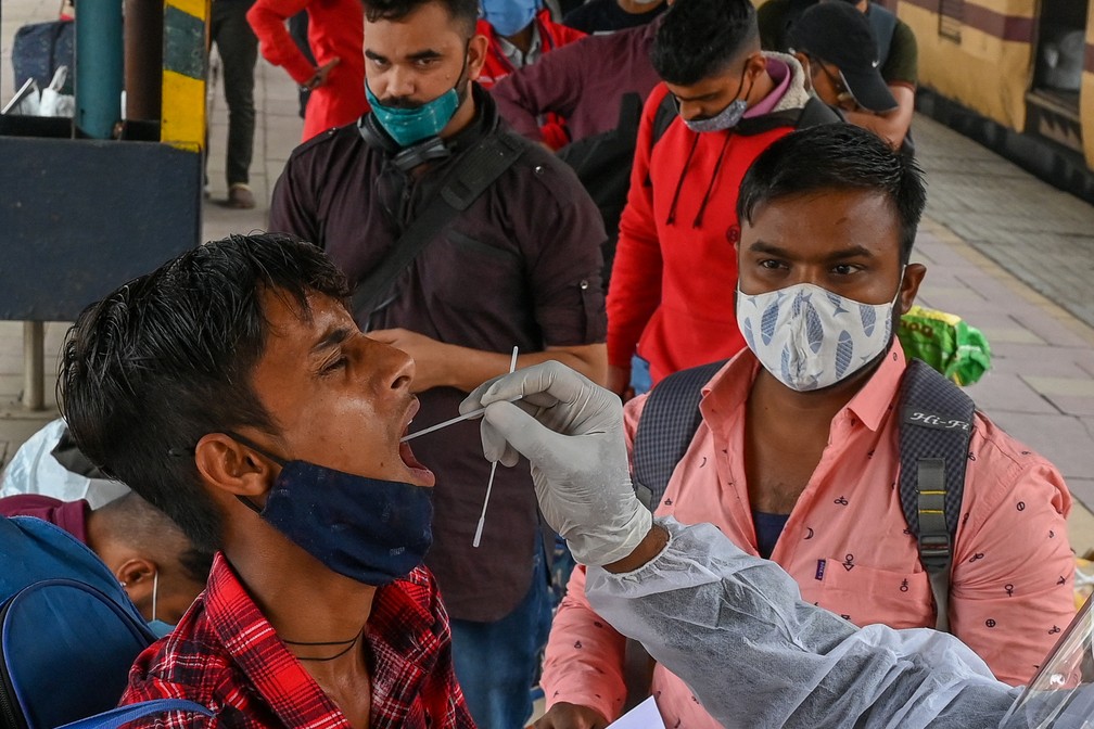 Profissional de saúde usando equipamento de proteção coleta amostra nasal de um passageiro para teste de Covid-19 em uma plataforma ferroviária em Mumbai, na Índia, nesta sexta-feira (7). — Foto: Punit Paranjpe / AFP