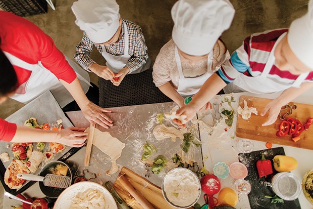 Photo of a cute little children preparing pizza in the kitchen, with a little help from their mom (Foto: Getty Images)
