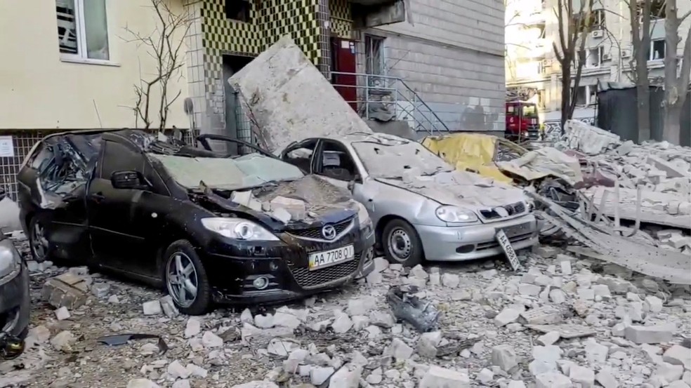 Carros ficam danificados e cobertos por detritos após prédio residencial em Kiev, capital da Ucrânia, ser atingido por bombardeio em 16 de março de 2022 — Foto: Serviço de Emergência da Ucrânia/Reuters
