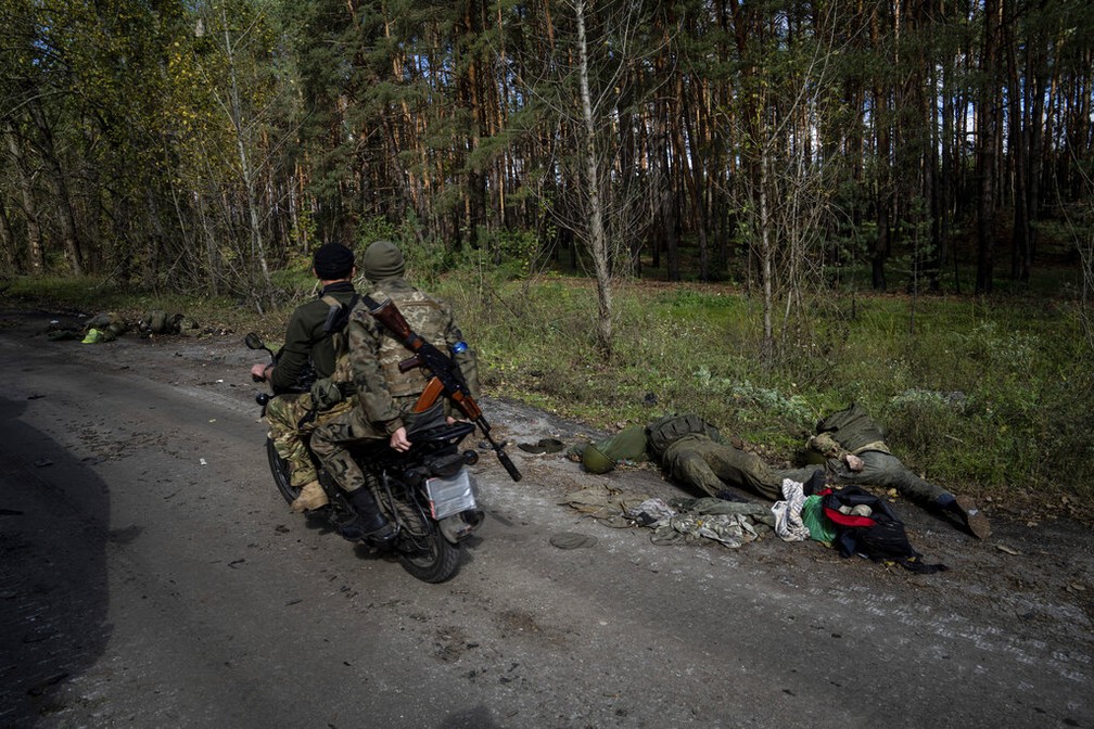 Soldados ucranianos, de moto, perto de corpos de russos, em 4 de outubro de 2022 — Foto: Evgeniy Maloletka/AP