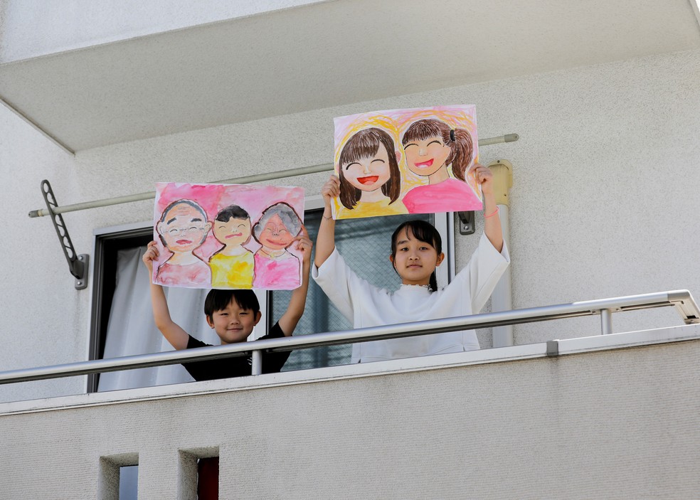 Reku Matsui, de 8 anos, e Yaya Matsui, de 12 anos, posam para uma foto enquanto seguram fotos tiradas durante o surto de doença por coronavírus (COVID-19) na varanda de sua casa em Tóquio, no Japão — Foto: Kim Kyung-Hoon/Reuters