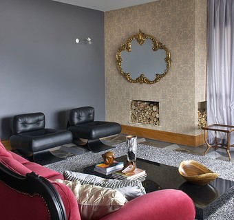 A sala decorada pelo designer Marcelo Rosenbaum tem papel de parede adamascado dourado em torno da lareira. A moldura do espelho também leva o tom