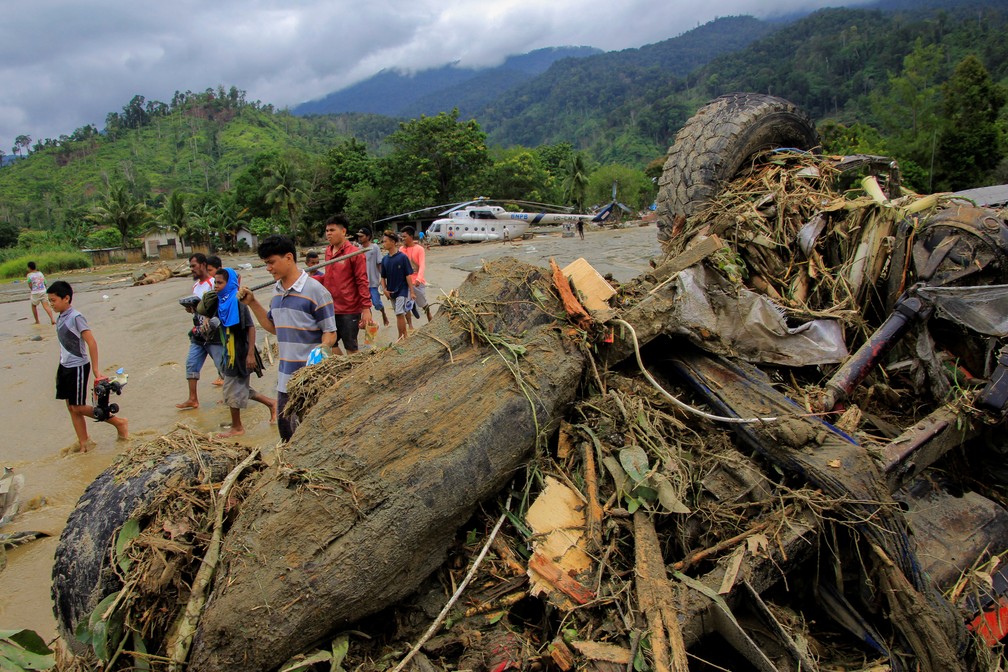 Pessoas caminham perto de carro danificado pela enchente em Papua, na Indonésia — Foto: Gusti Tanati/Antara Foto via Reuters