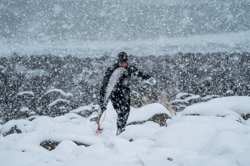 Surfista carrega a prancha no meio de uma tempestade de neve em 11 de março  (Foto: Olivier Morin/AFP)