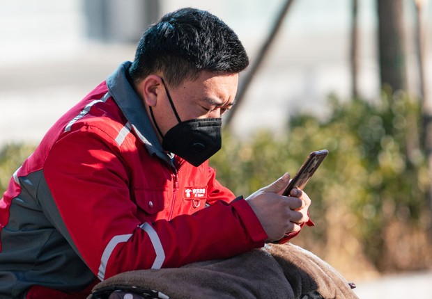 Um homem com uma máscara facial usa um telefone celular, na China (Foto: Artyom Ivanov / Colaborador via Getty Images)